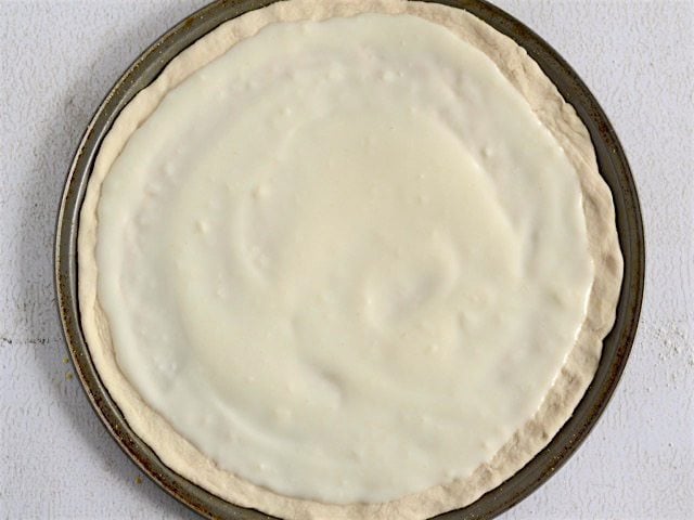 White sauce spread onto pizza dough