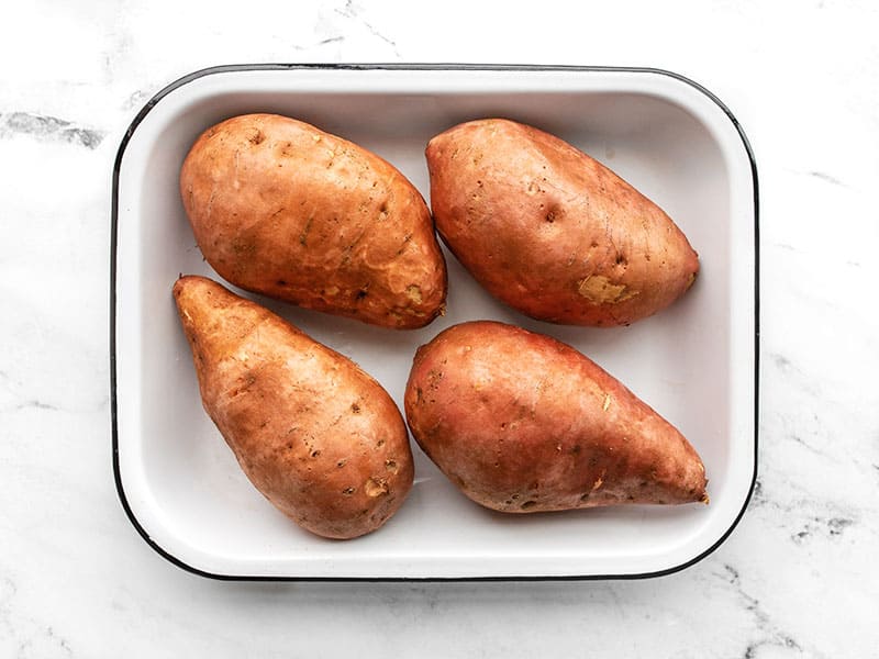 Sweet potatoes in a baking dish rubbed in oil and pricked with a fork