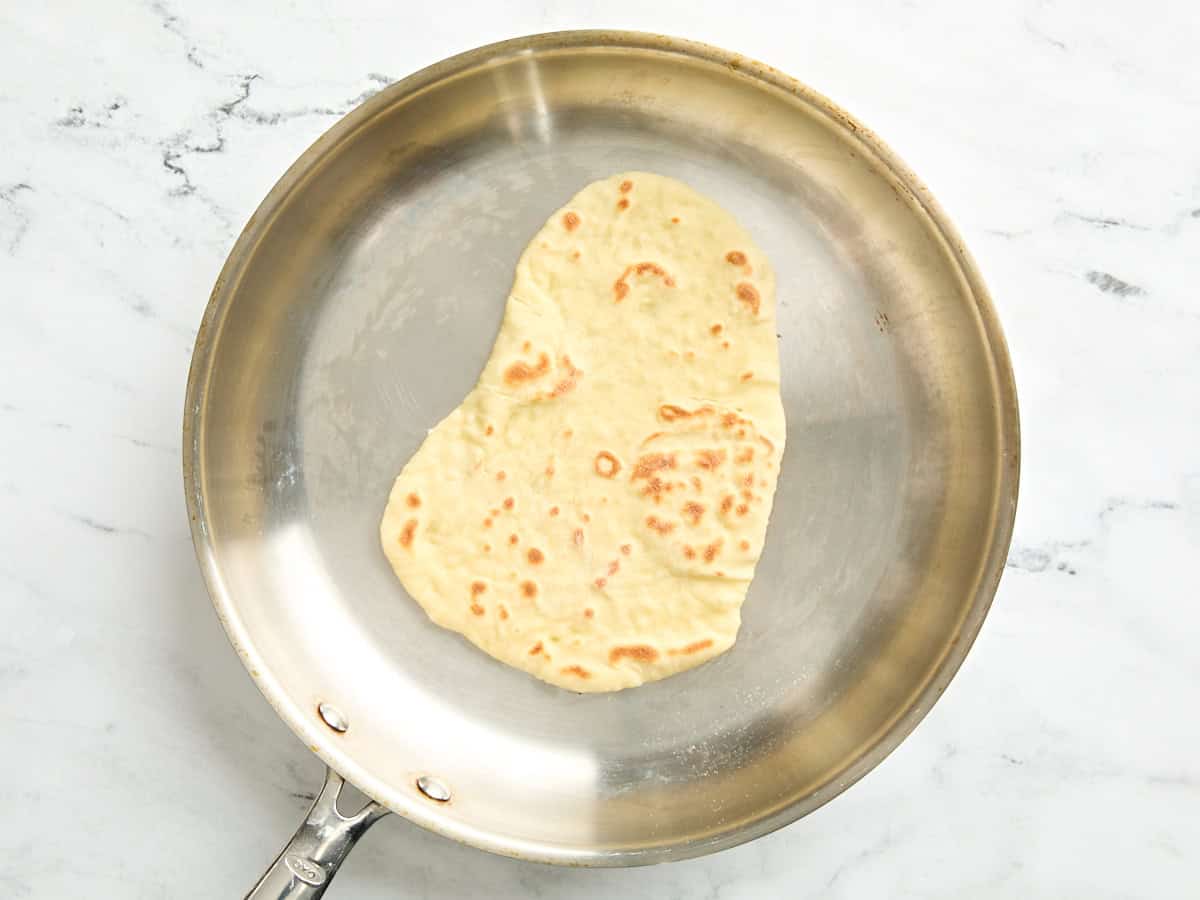 A browned naan cooking in a skillet.