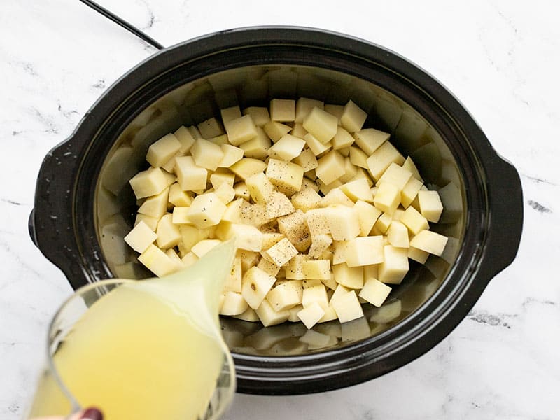 Chicken broth being poured into the slow cooker with potatotes