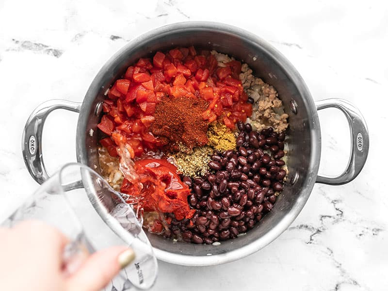 Tomatoes, beans, spices, and water added to the pot.