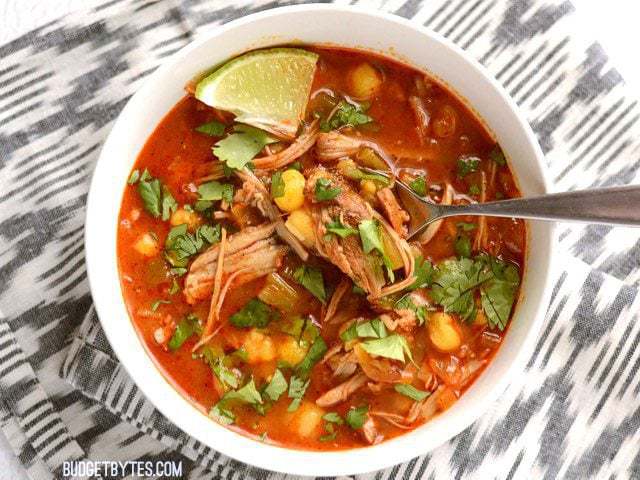 Bird's eye view of a bowl of 30 Minute Posole with a spoon full of pork and hominy,