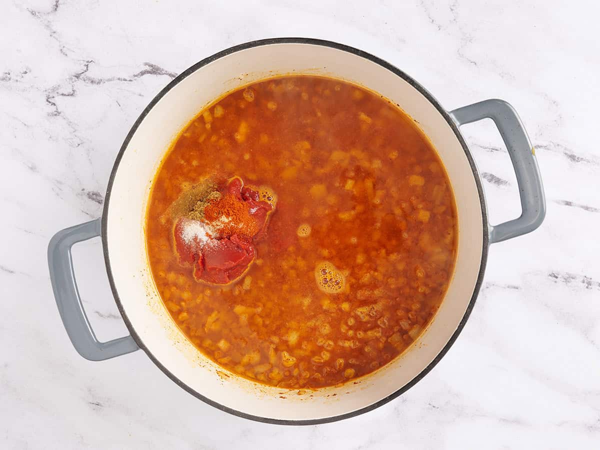 Tomato paste, seasonings, and water added to sauteed onions in a pot.