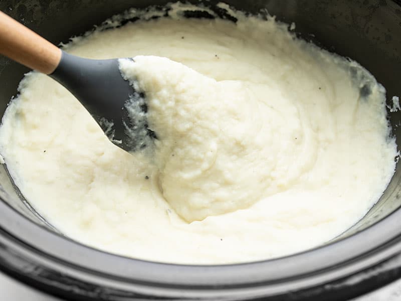 Creamy mashed potatoes in the slow cooker with a spoon, close up