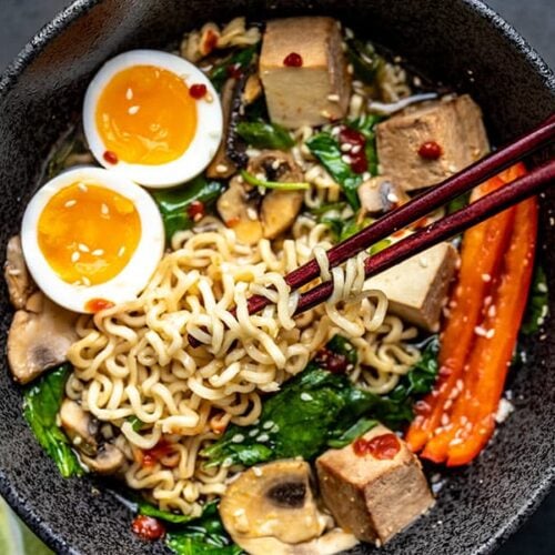 Close up of Chopsticks lifting noodles out of an upgraded bowl of instant ramen, with a soft boiled egg.