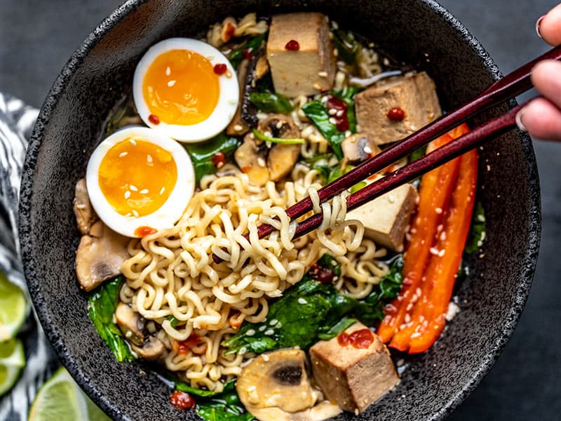 Close up of Chopsticks lifting noodles out of an upgraded bowl of instant ramen, with a soft boiled egg.