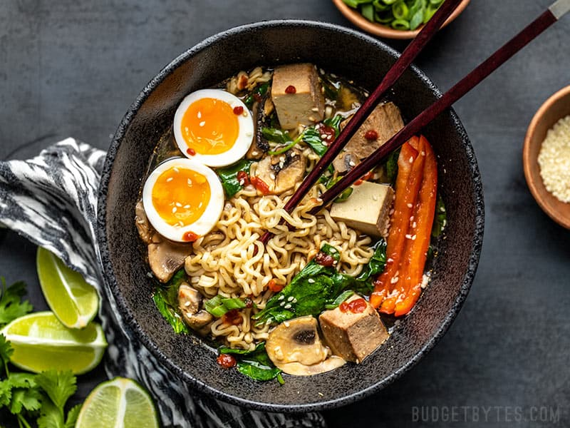 An upgraded bowl of instant ramen, viewed from above, being eaten with chopsticks