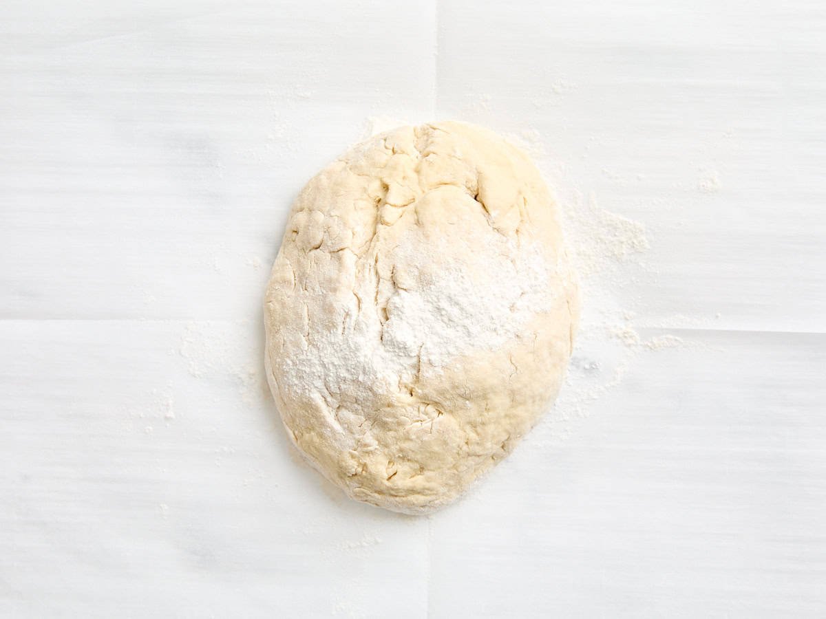 A ball of naan dough on a floured surface sprinkled with flour.