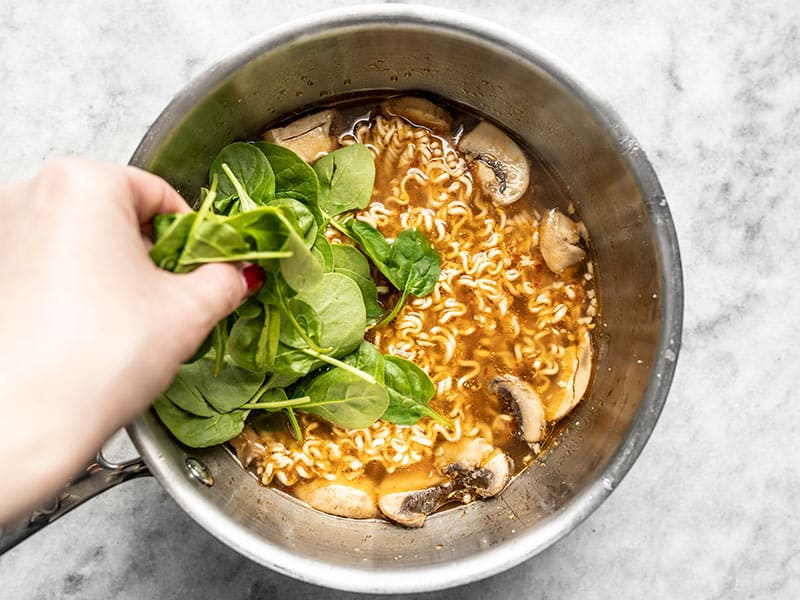 Spinach being added to cooked ramen in the sauce pot.