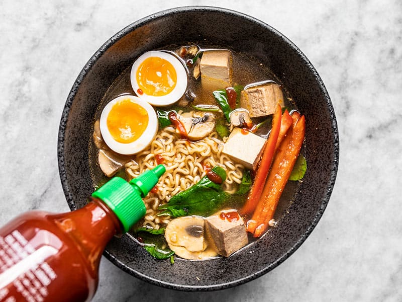 Sriracha being drizzled on a bowl of upgraded Instant Ramen.