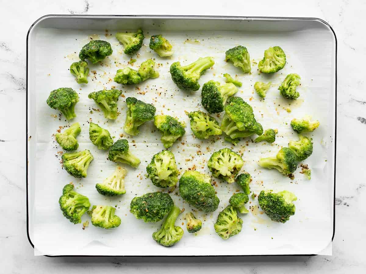 Seasoned broccoli florets on a baking sheet lined with parchment paper