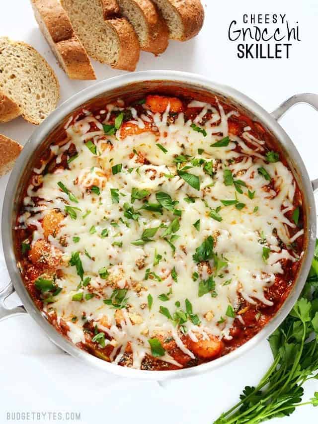 Overhead view of a skillet full of cheesy gnocchi, sliced bread and parsley on the sides