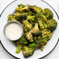 a plate full of oven roasted frozen broccoli and a cup of ranch dressing
