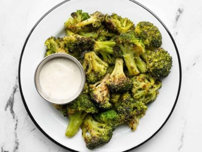 a plate full of oven roasted frozen broccoli and a cup of ranch dressing