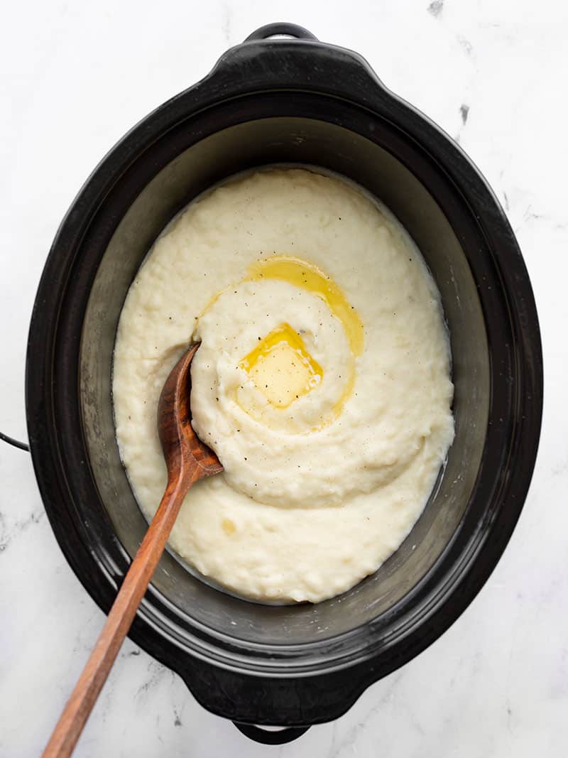Slow Cooker Mashed Potatoes in the slow cooker with melted butter and a wooden spoon