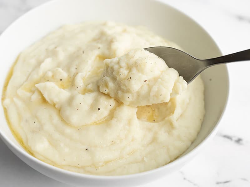 Slow cooker mashed potatoes in a bowl with a spoon lifting a bite