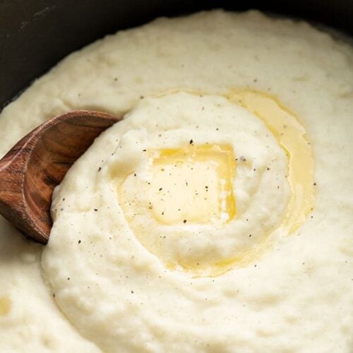 Close up of mashed potatoes in the slow cooker with melted butter and a wooden spoon