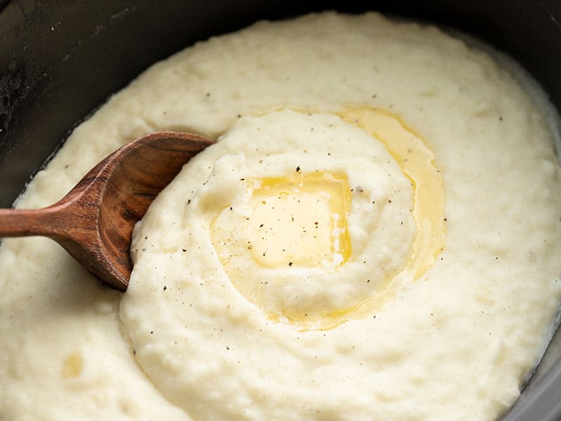 Close up of mashed potatoes in the slow cooker with melted butter and a wooden spoon