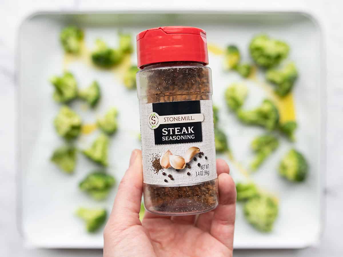 Close up of a bottle of steak seasoning with the broccoli in the background
