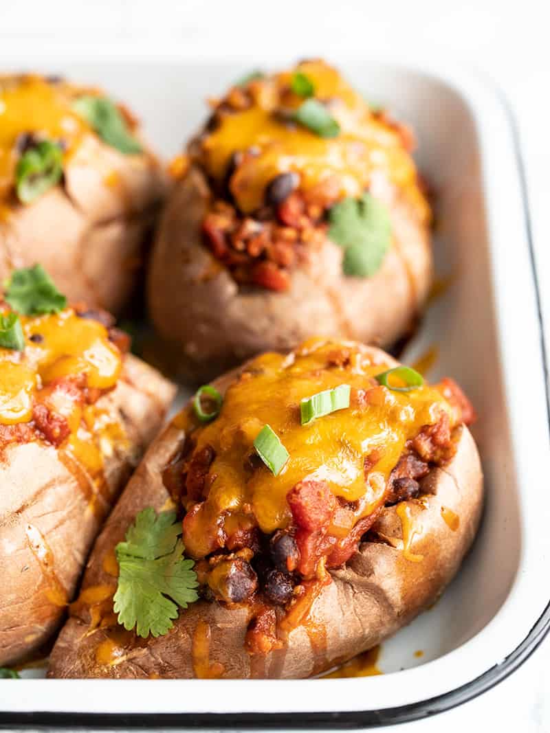 Front view of four turkey chili stuffed sweet potatoes in a small white baking dish