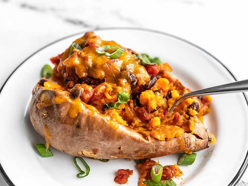 A fork digging into a turkey chili smothered sweet potato, on a white plate