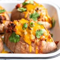 Side view of turkey chili smothered sweet potatoes in a baking dish, topped with green onion and cilantro