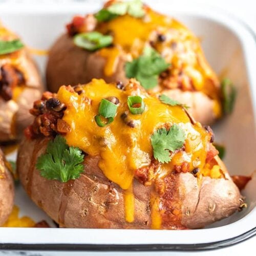 Side view of turkey chili smothered sweet potatoes in a baking dish, topped with green onion and cilantro