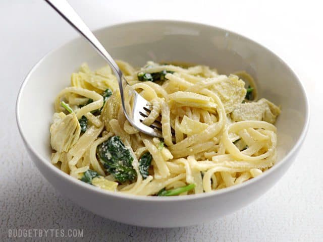 Side view of a bowl of creamy spinach artichoke pasta with a fork in the center