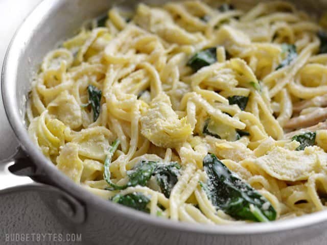 Close up side view of the skillet full of creamy spinach artichoke pasta