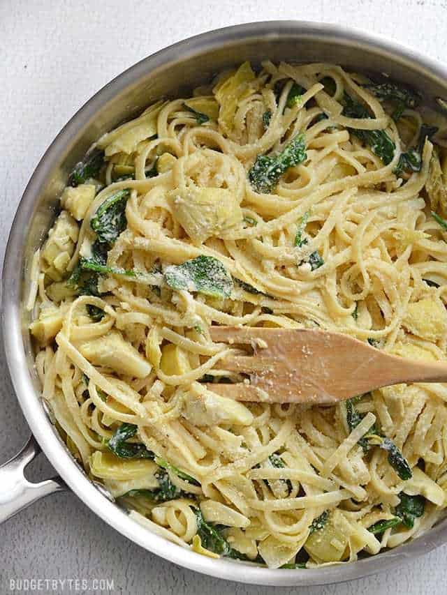 Overhead view of Creamy Spinach Artichoke Pasta in the skillet with a wooden pasta fork