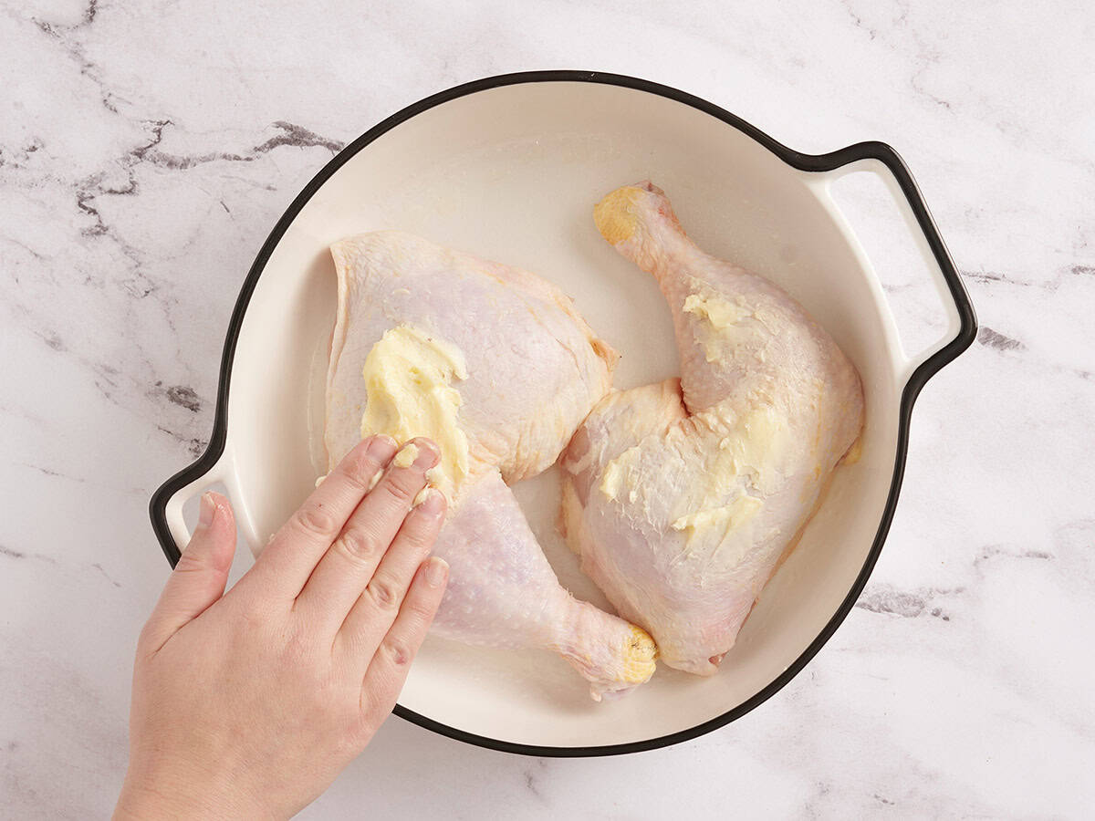 A hand rubbing butter over a chicken leg.