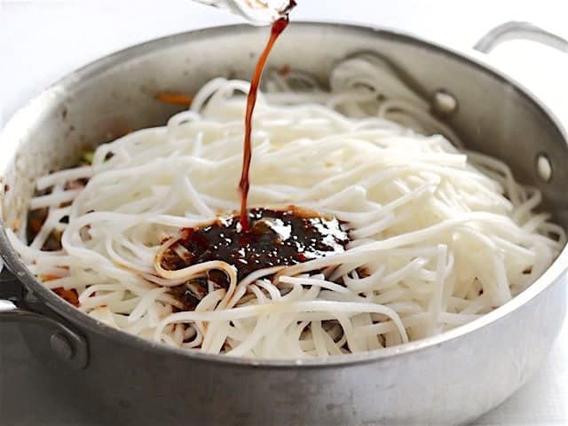 Cooked noodles in the skillet, stir fry sauce being poured over top