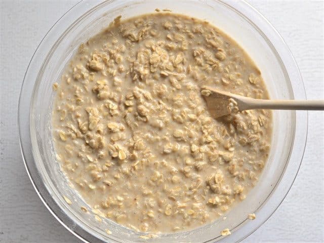 rolled oats stirred into batter in the mixing bowl, with a wooden spoon