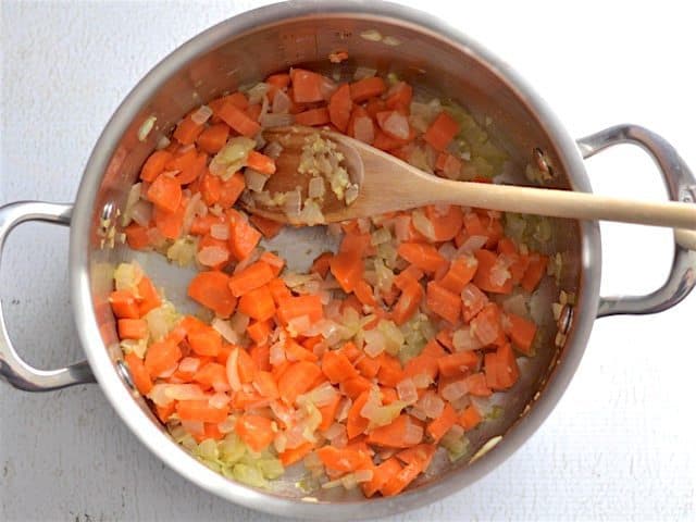 Carrots added to the soup pot, a wooden spoon in the pot