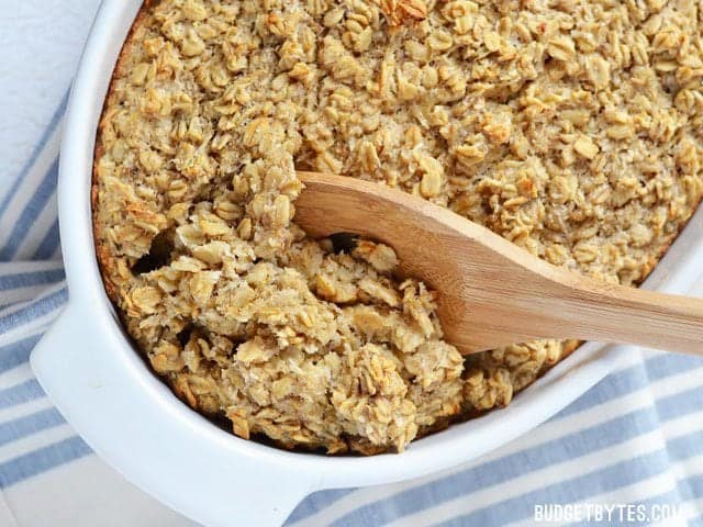 Banana Coconut Baked Oatmeal in a casserole dish being scooped out with a wooden spoon