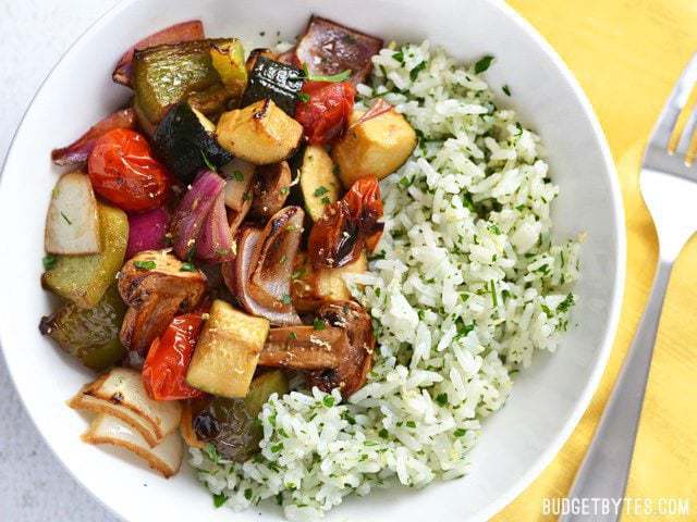 Broiled balsamic vegetables top a vibrant and fresh lemon parsley rice to make this light and healthy dish. Works great as a side or a light meal. Budetbytes.com Finished bowl of Broiled Balsamic Vegetables with Lemon Parsley Rice on a yellow napkin, fork on the side