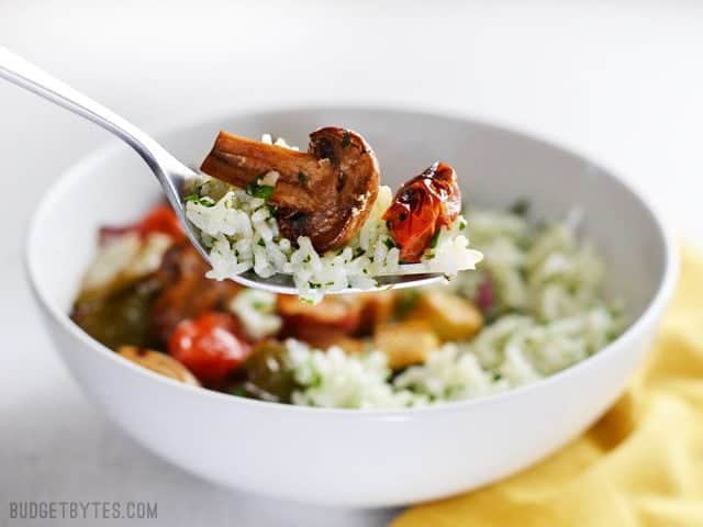 Broiled balsamic vegetables top a vibrant and fresh lemon parsley rice to make this light and healthy dish. Works great as a side or a light meal. Budetbytes.com A forkful of Broiled Balsamic Vegetables with the bowl of Lemon Parsley Rice in the background