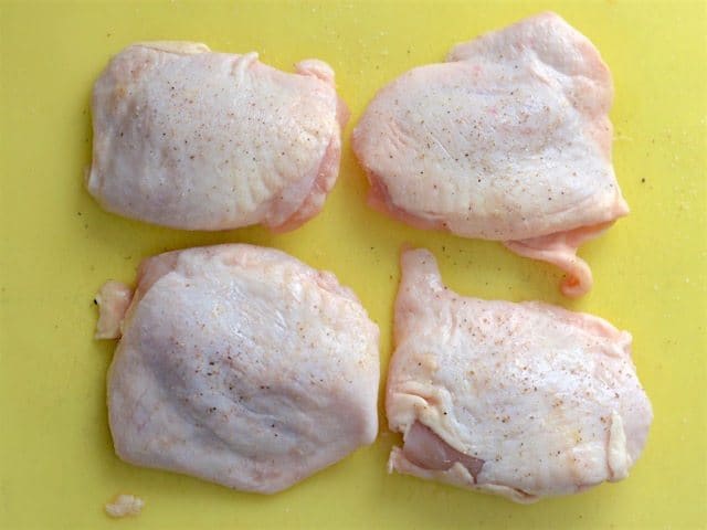 Raw Chicken Thighs on a cutting board, seasoned with salt and pepper