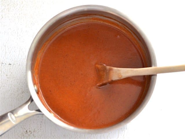 Finished enchilada sauce in the sauce pot with a wooden spoon