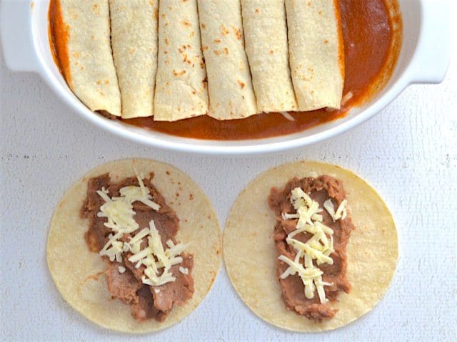 Tortillas being filled, rolled, and placed in a casserole dish with enchilada sauce