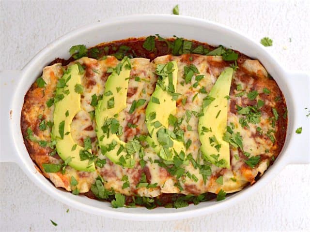 These easy Bean and Cheese Enchiladas are anything but boring. A few extra details take them from a simple to spectacular weeknight dinner. BudgetBytes.com Finished Weeknight Enchiladas, topped with avocado and cilantro