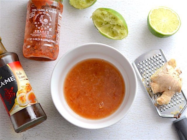 Nam Sod Dressing in a small white bowl, ginger, lime, chili garlic sauce, and fish sauce on the side