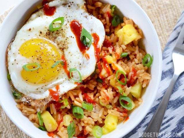 Use up the leftovers in your fridge with these fast and tasty Pineapple Sriracha Breakfast Bowls. Easy and customizable to fit what you have on hand. Budetbytes.com Close up overhead view of a pineapple sriracha breakfast bowl with a fried egg on top