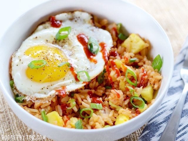 Side view of a Pineapple Sriracha Breakfast Bowls garnished with sriracha and green onion, a fork on the side