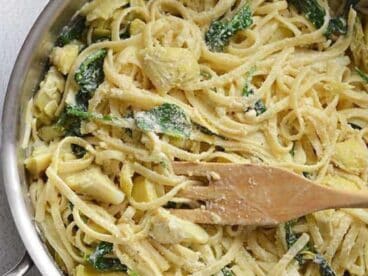 Creamy Spinach and Artichoke Pasta in a pot with a wooden spoon.