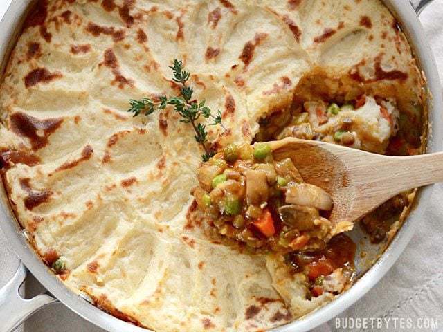 Close up of Vegetarian Shepherd's Pie in the skillet, a wooden spoon scooping out a serving