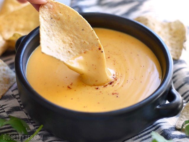 Chip dipping into a bowl of rich and creamy 5 Minute Nacho Cheese Sauce