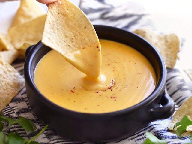 Chip dipping into a bowl of nacho cheese sauce.