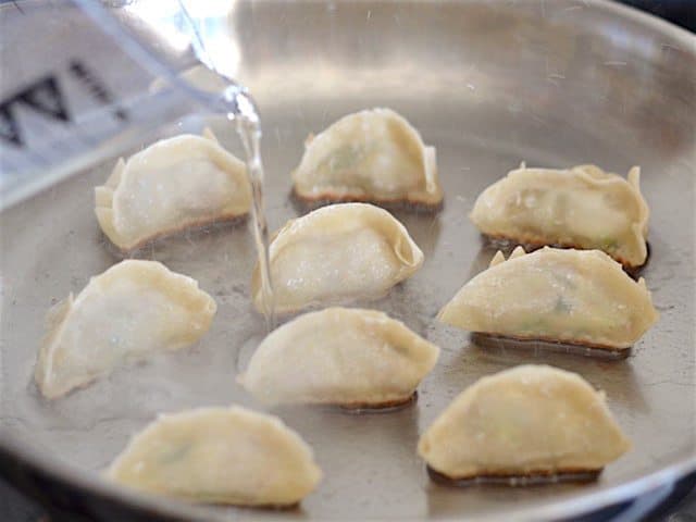 Water being poured into the skillet with the fried pork gyoza