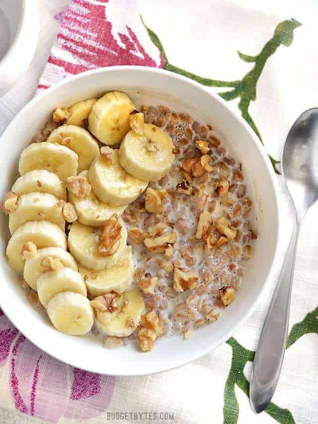 A bowl of Banana Nut Breakfast Farro with sliced banana on top, the bowl on a floral cloth napkin